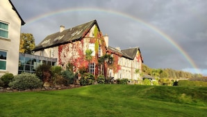 A large house with a garden in front, a rainbow in the sky, and a stone wall. - Best Western Balgeddie House Hotel (Glenrothes)
