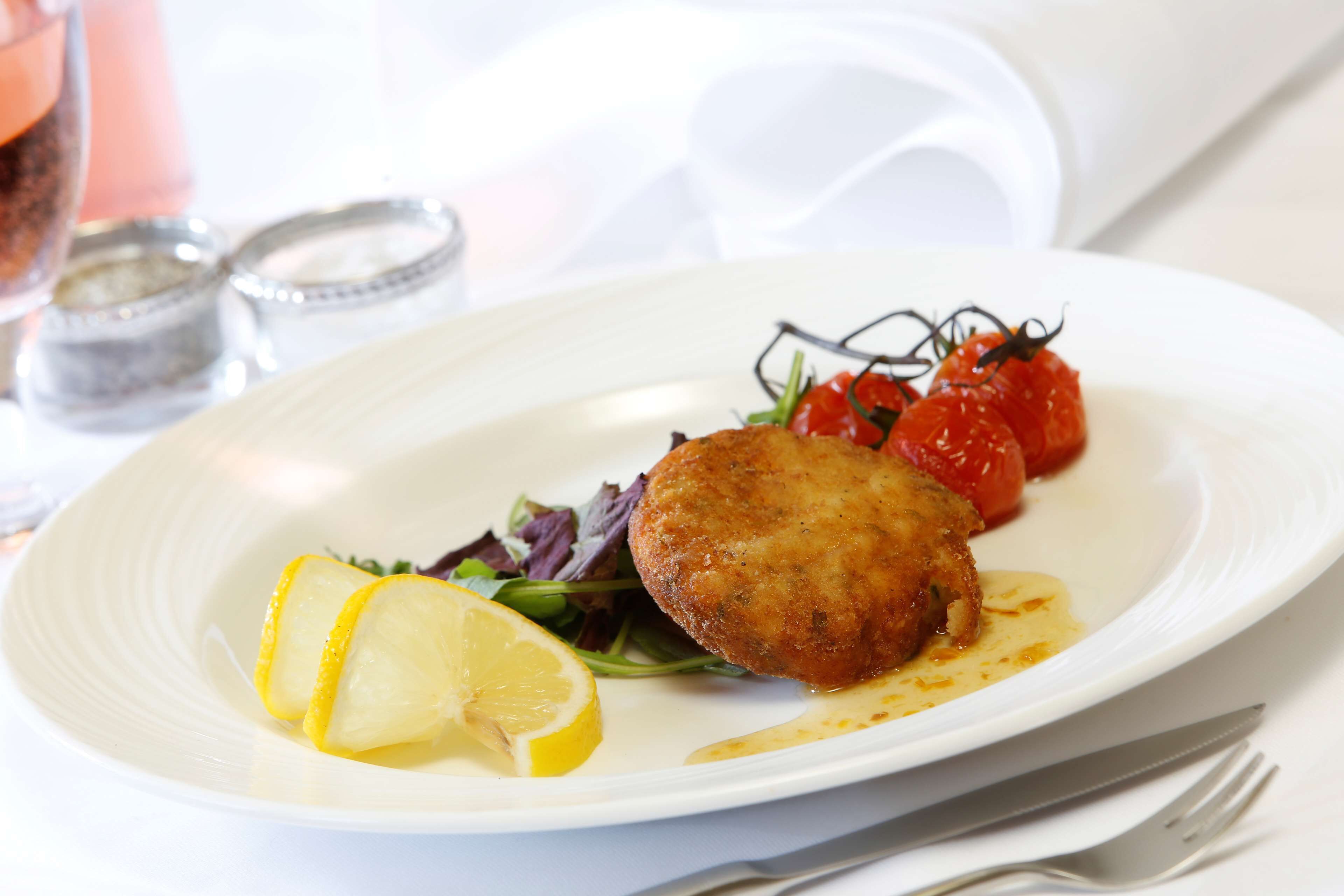 A plate with a breaded item, lemon slices, and a salad.