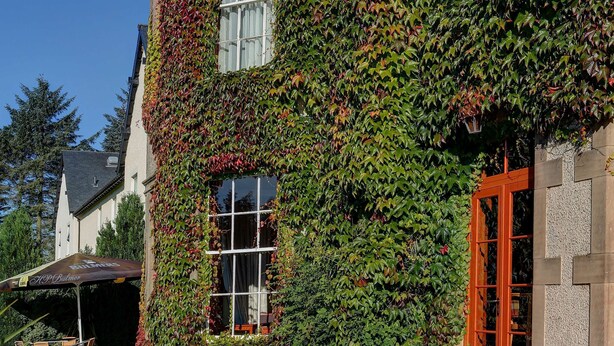A building with ivy-covered walls and a glass door. There are outdoor tables and chairs arranged for dining. - Best Western Balgeddie House Hotel (Glenrothes)