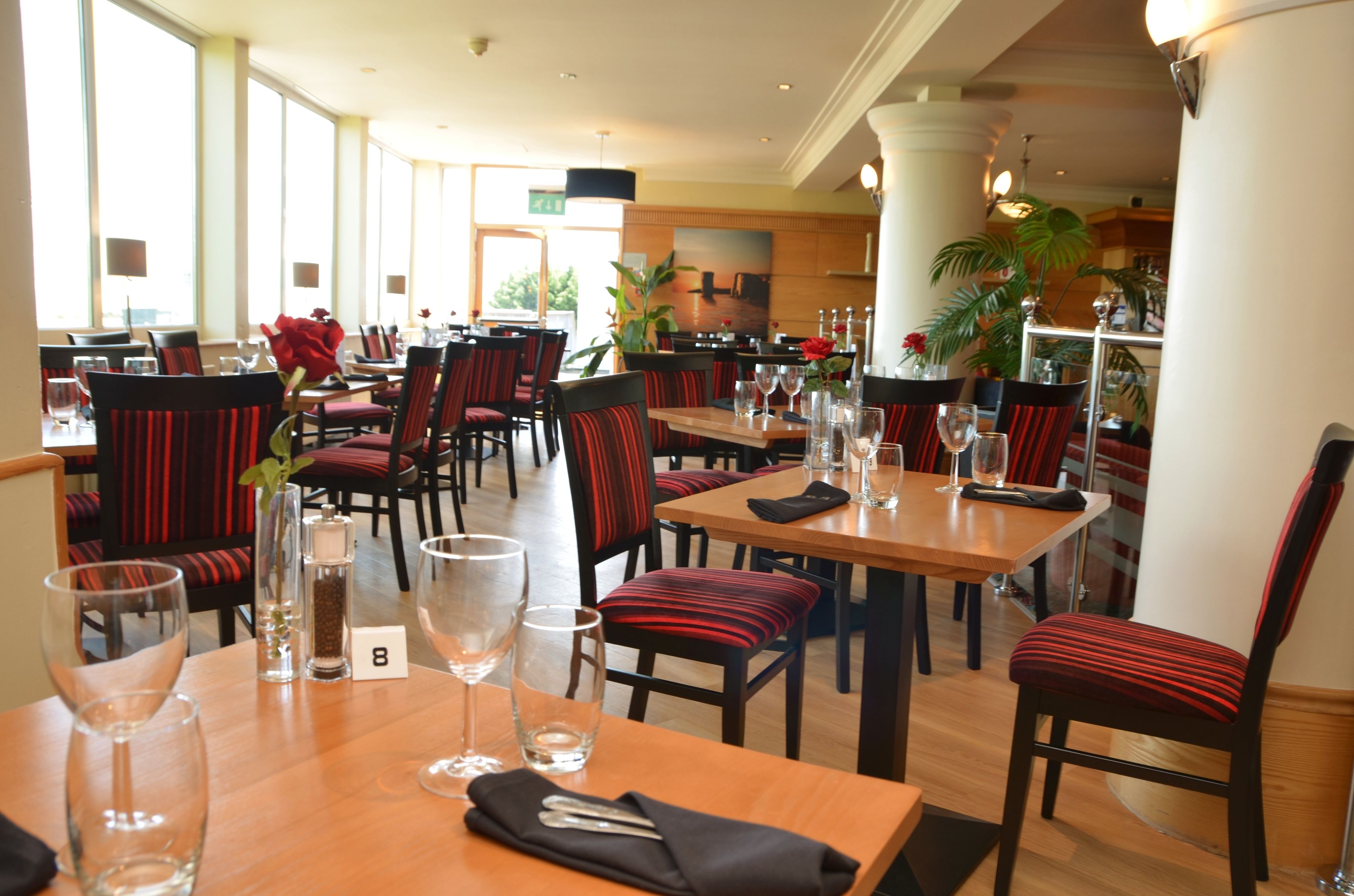 A restaurant with tables set for dining, chairs with red cushions, and a number 8 sign on a table.