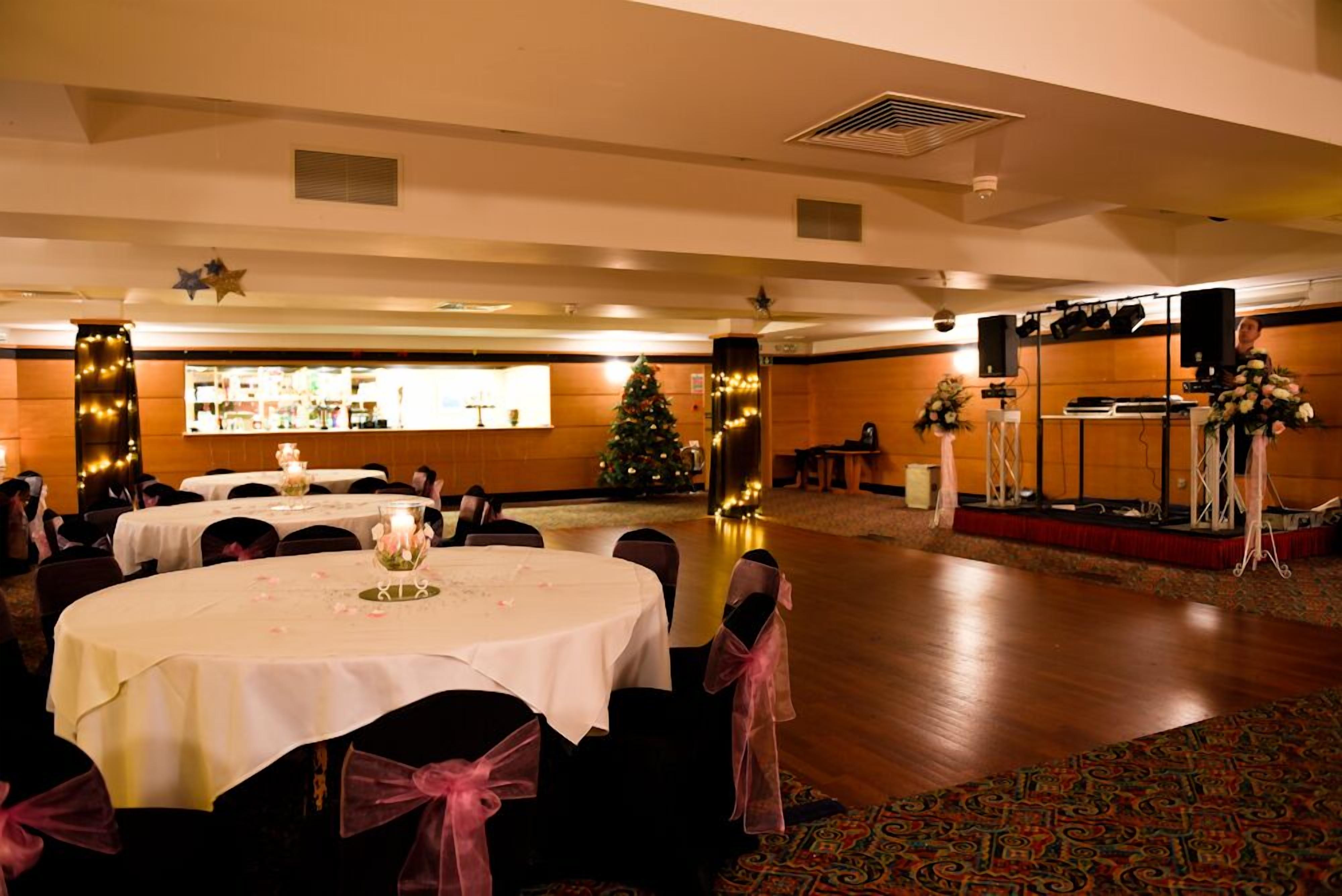A banquet hall with round tables, chairs, and a stage with speakers.