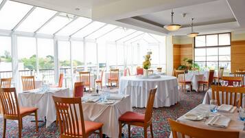 Un restaurante con mesas redondas, sillas de madera y una alfombra estampada.