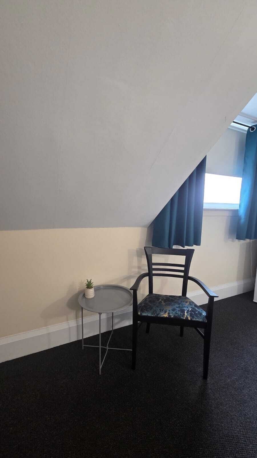 Um quarto com uma cadeira preta, uma mesa redonda pequena e um vaso com planta.