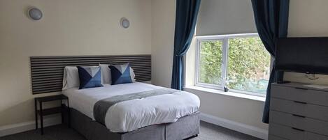 A bedroom with a bed, a dresser, a window with curtains, and a wall-mounted light fixture.