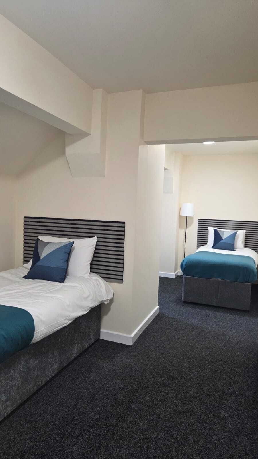 A hotel room with two beds, a dark carpet, and a modern design.