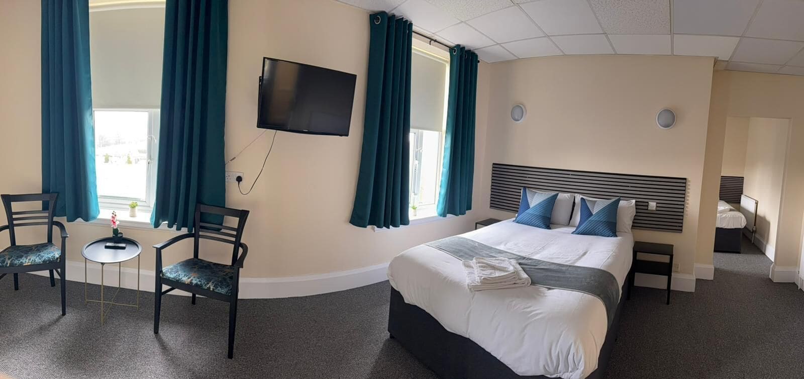 Une chambre d’hôtel comprenant un lit, un téléviseur fixé au mur, un bureau avec une chaise et une fenêtre avec des rideaux.