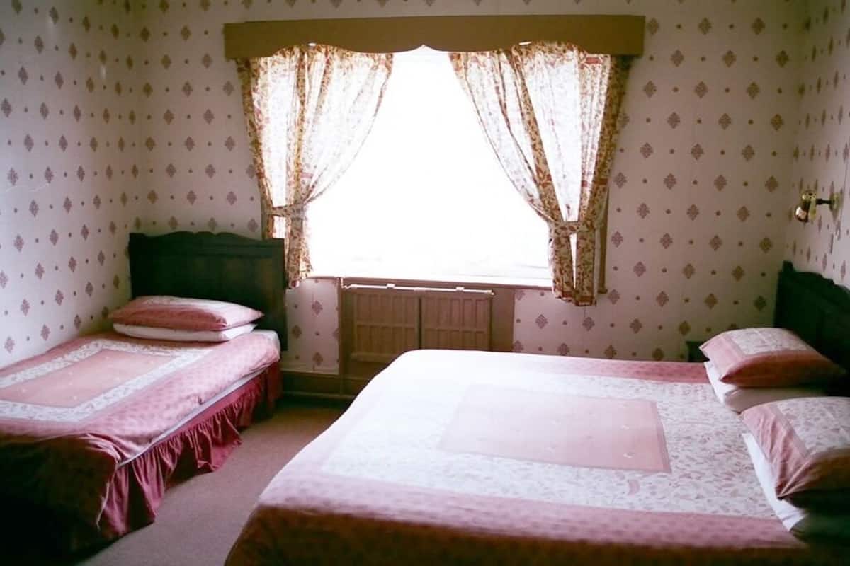 A room with two single beds, a radiator, and a window with curtains.