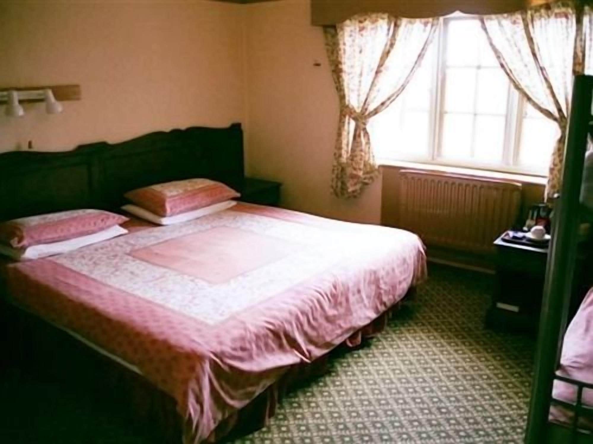 A bedroom with a bed, a nightstand, a radiator, and a window with curtains.