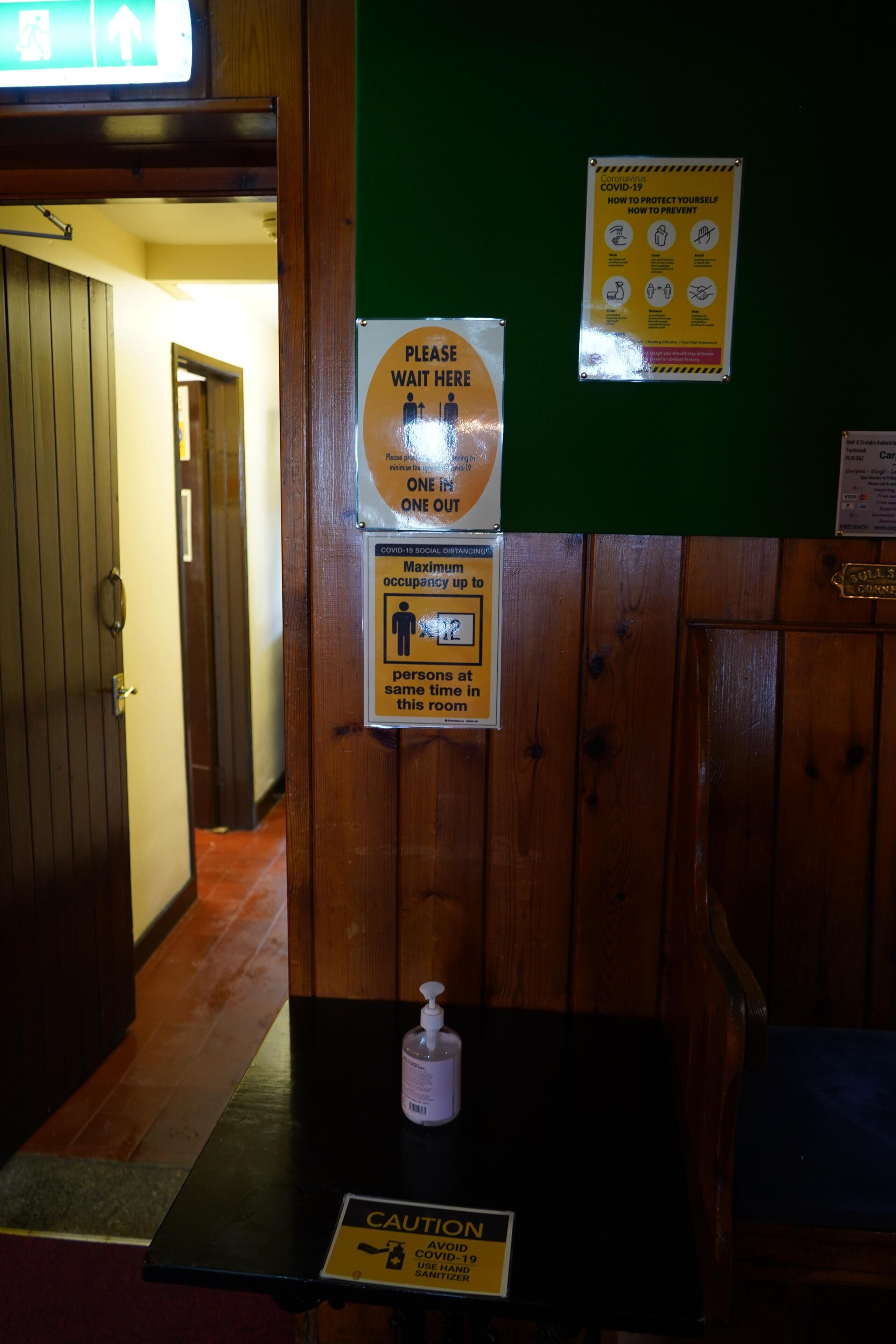 Un intérieur en bois avec des panneaux indiquant les mesures de distanciation sociale liées à la COVID-19, un flacon de désinfectant sur une table et un panneau d’avertissement concernant la COVID-19.