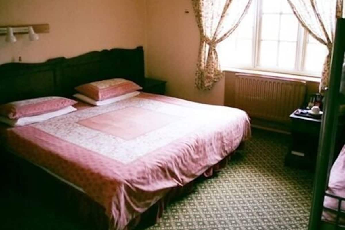 A single bed with a headboard, a bedside table, and a window with curtains.