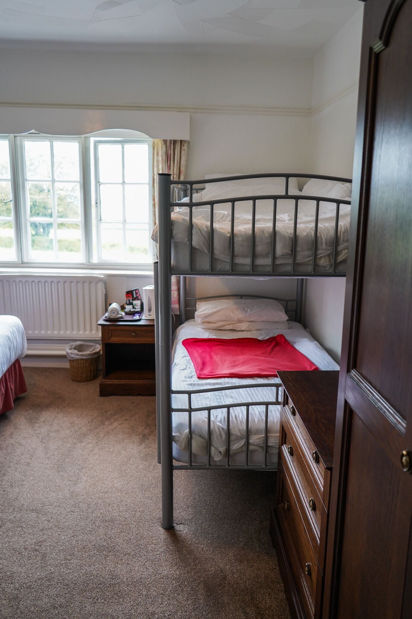 A bedroom with a bunk bed, a wooden dresser, a nightstand, and a window with curtains.