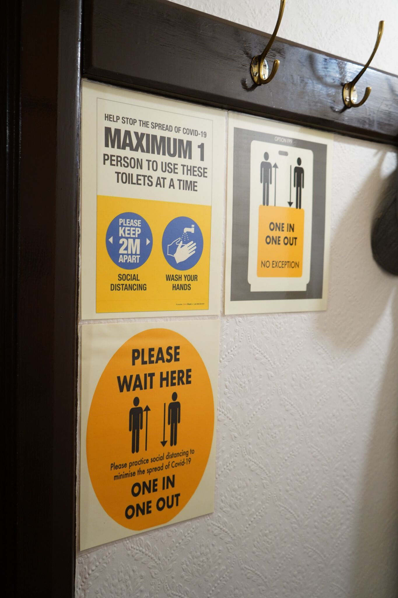 A wall with multiple signs instructing social distancing and one person per toilet.
