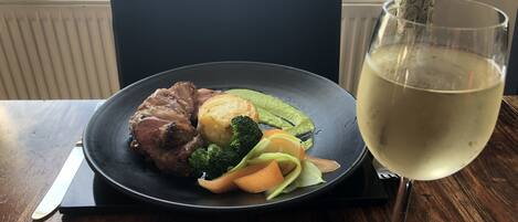 A plate of food with meat, vegetables, and a glass of white wine on a wooden table.