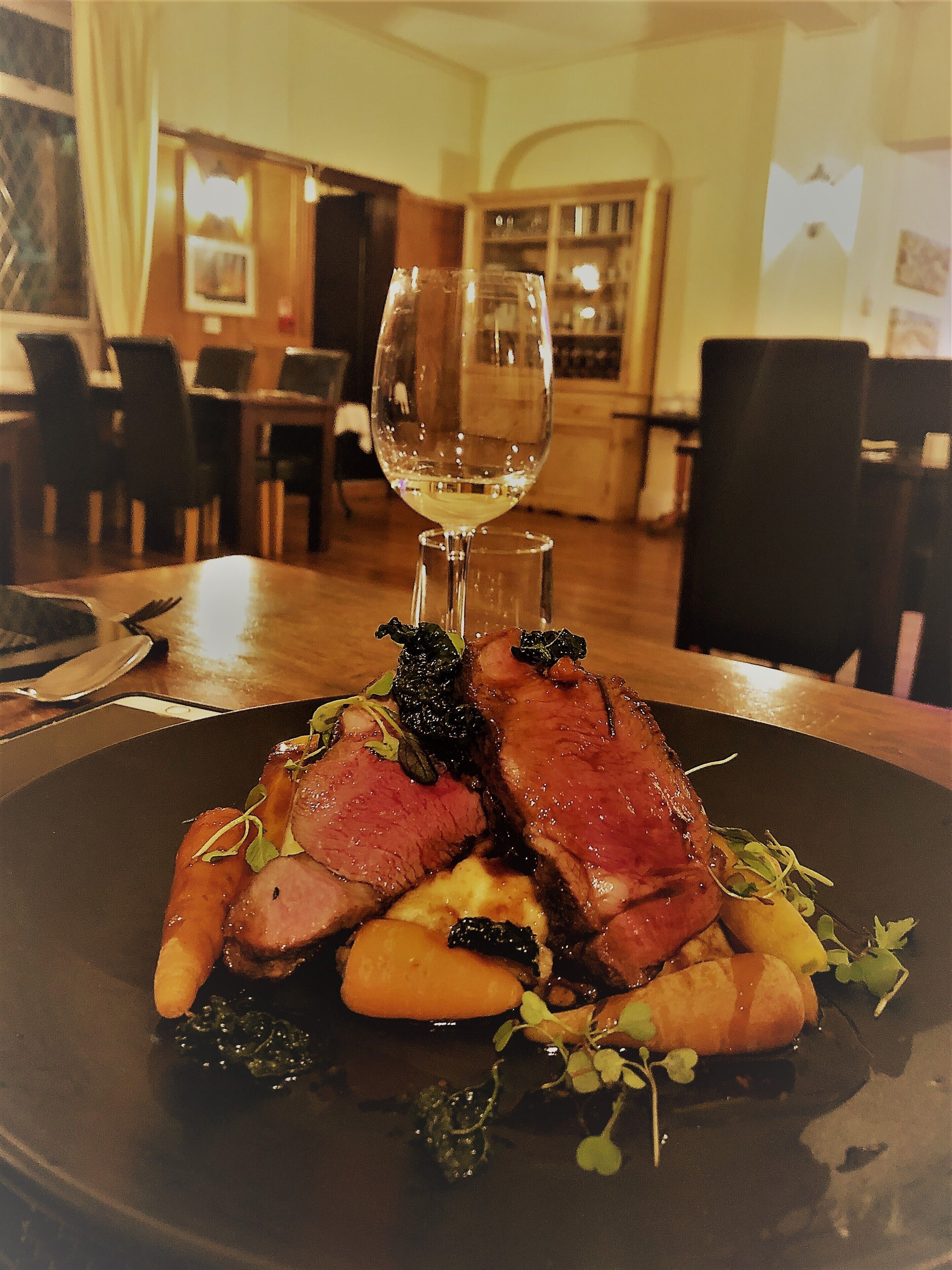Una mesa de comedor con un plato de comida, una copa de vino y una silla.