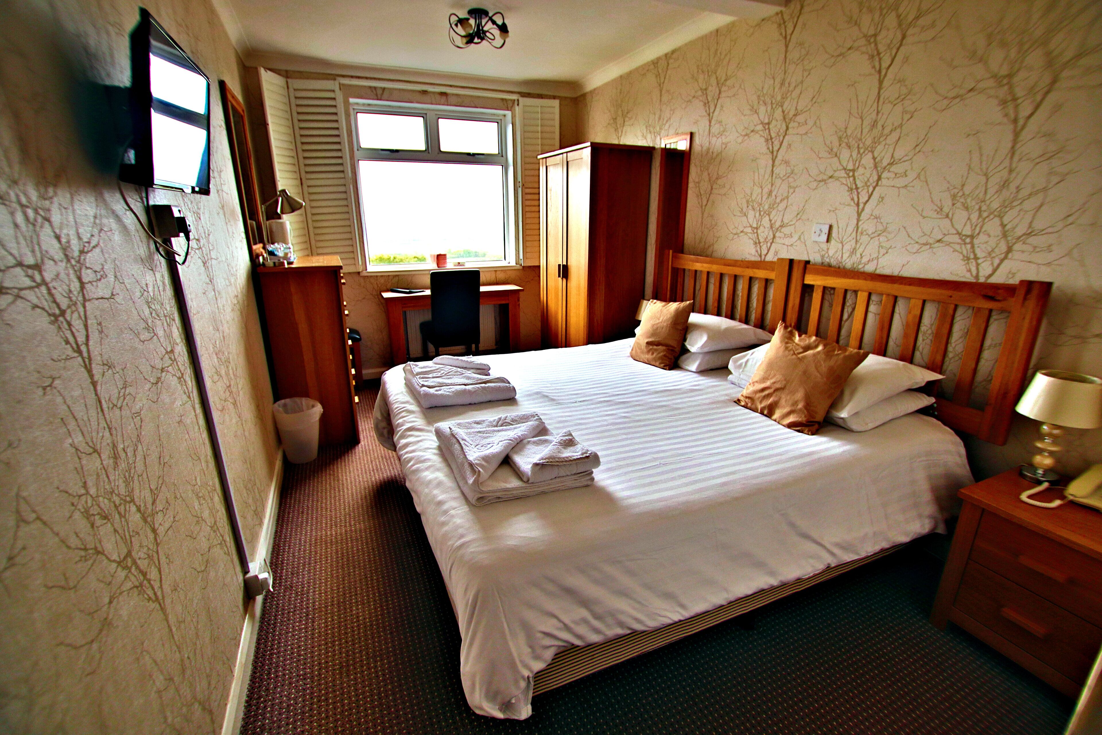 A hotel room with a bed, a desk, a chair, a wardrobe, and a television.