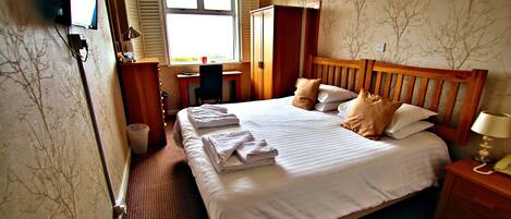 A hotel room with a bed, a desk, a chair, a wardrobe, and a television.