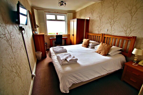 A hotel room with a bed, a desk, a chair, a wardrobe, and a television.