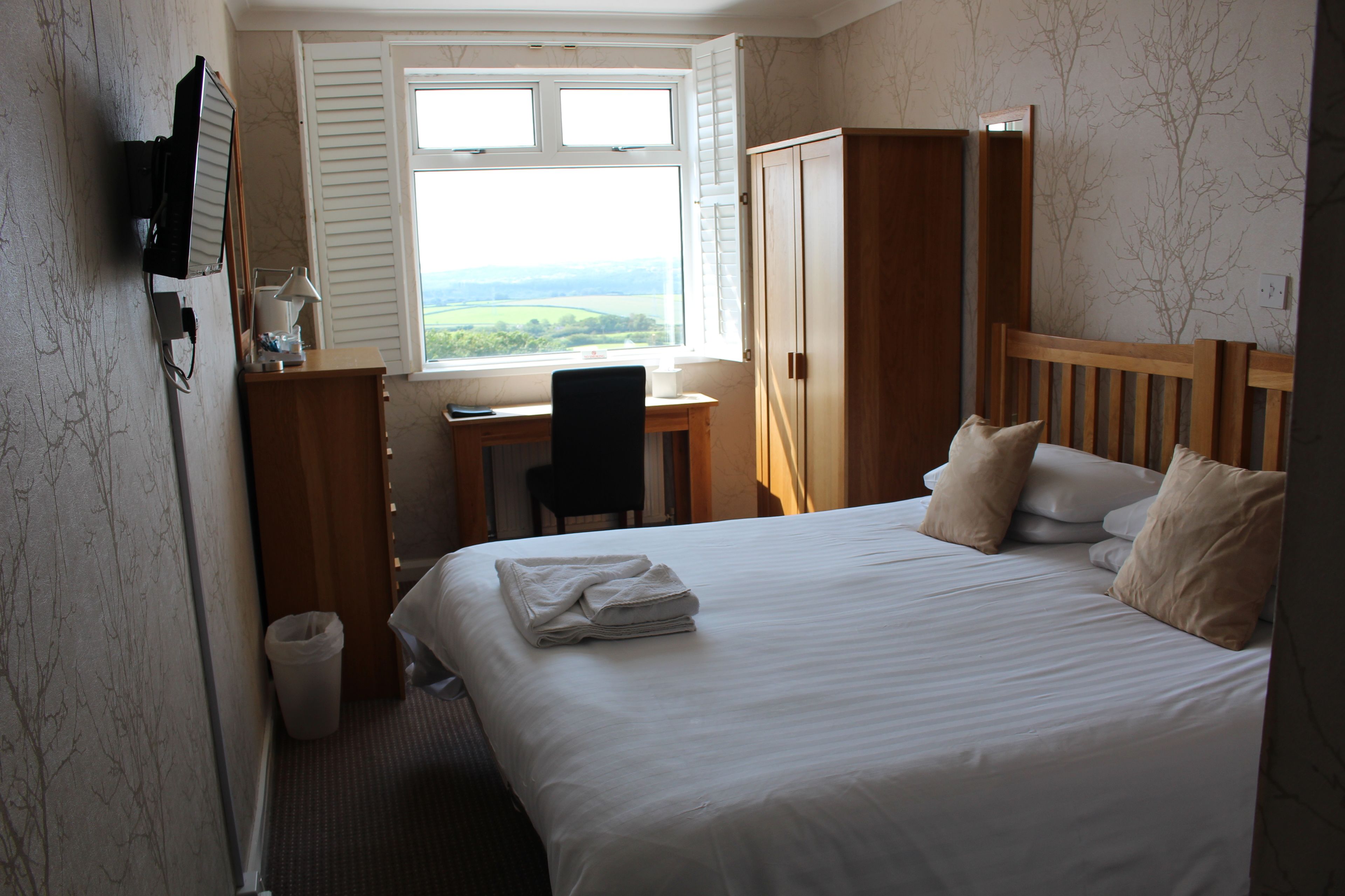 A hotel room with a bed, a desk, a chair, and a wardrobe.