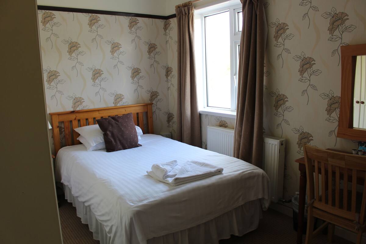 A neatly made bed with a wooden headboard, a bedside table, and a window with curtains.
