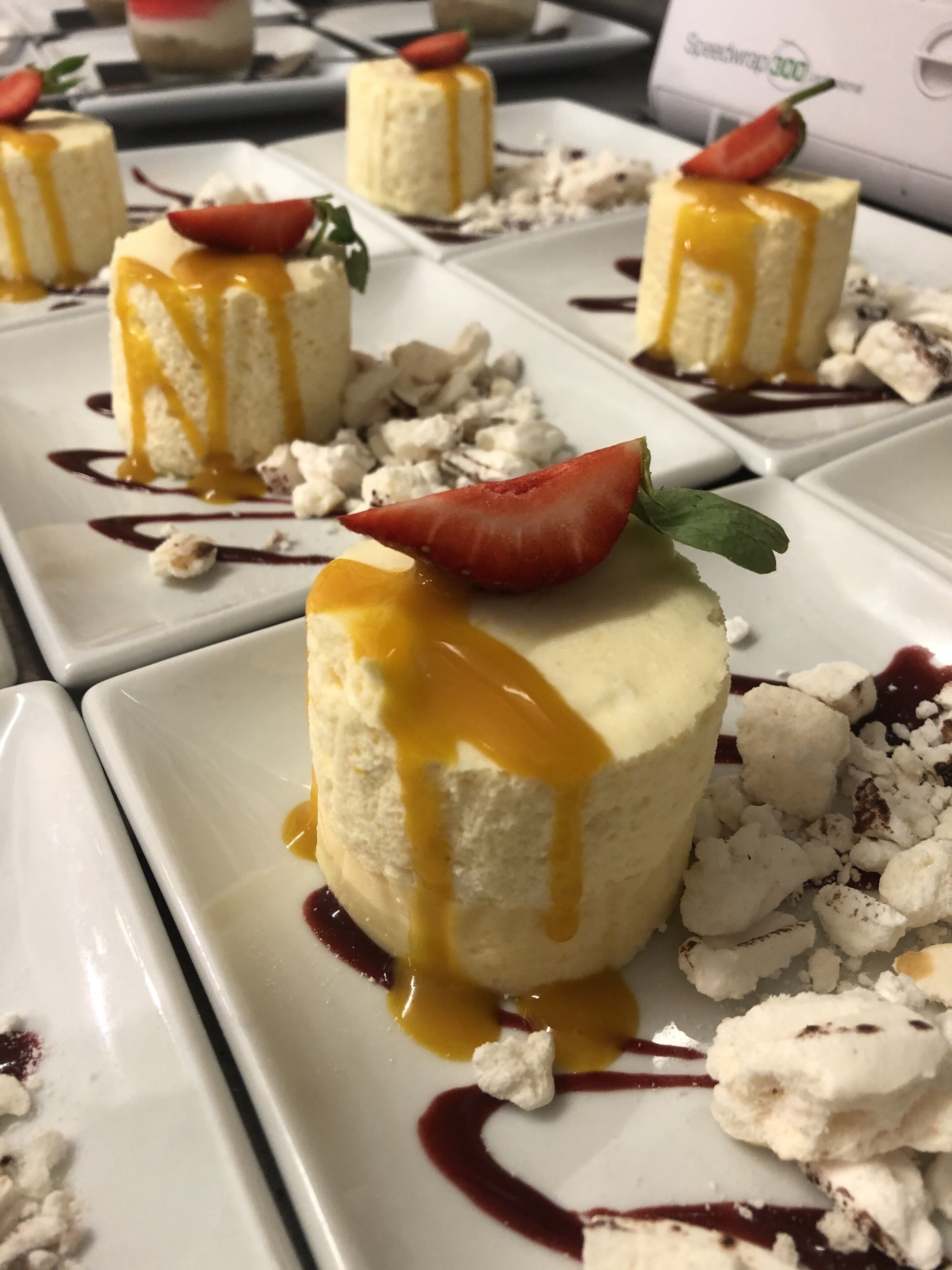 Un plato de postre con un dulce cremoso cubierto con fresa y rociado con salsa de caramelo.