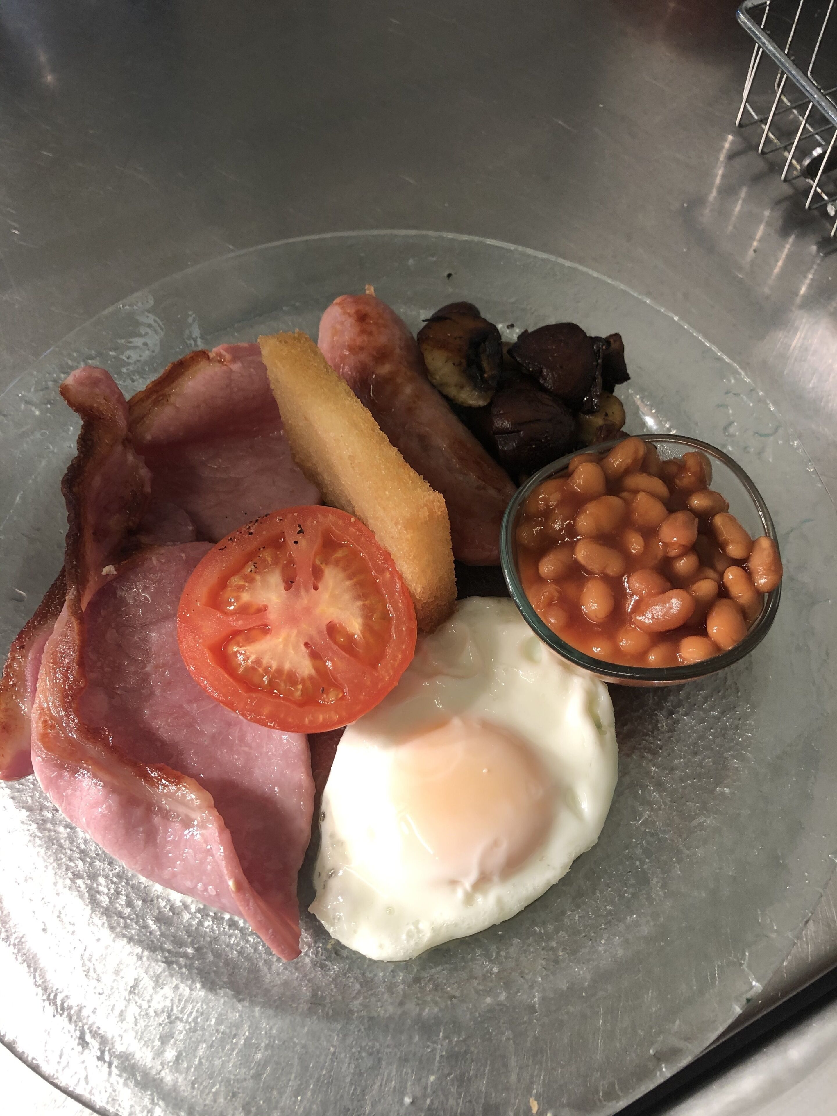 A breakfast plate with bacon, sausages, eggs, tomatoes, and baked beans.