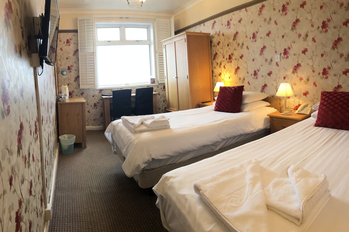 A hotel room with two beds, a desk, a wardrobe, and a window with shutters.