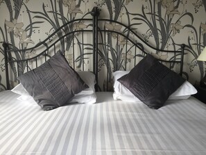 Una cama con ropa de cama a rayas, dos almohadas oscuras y un cabecero de metal con papel tapiz floral.