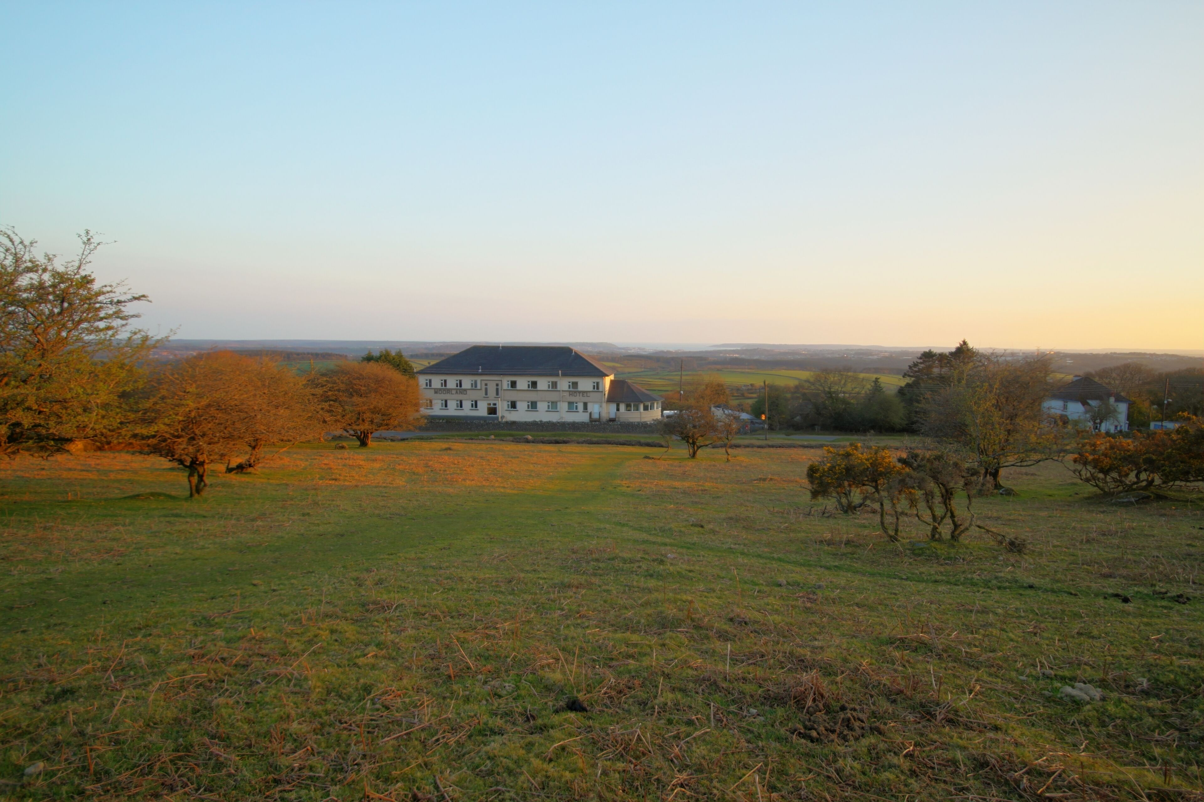 A large, white building with a symmetrical facade and a central entrance, surrounded by open fields and scattered trees.