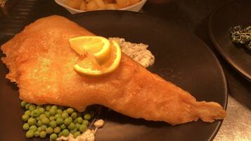 A plate with a piece of fried fish, peas, and a lemon wedge.