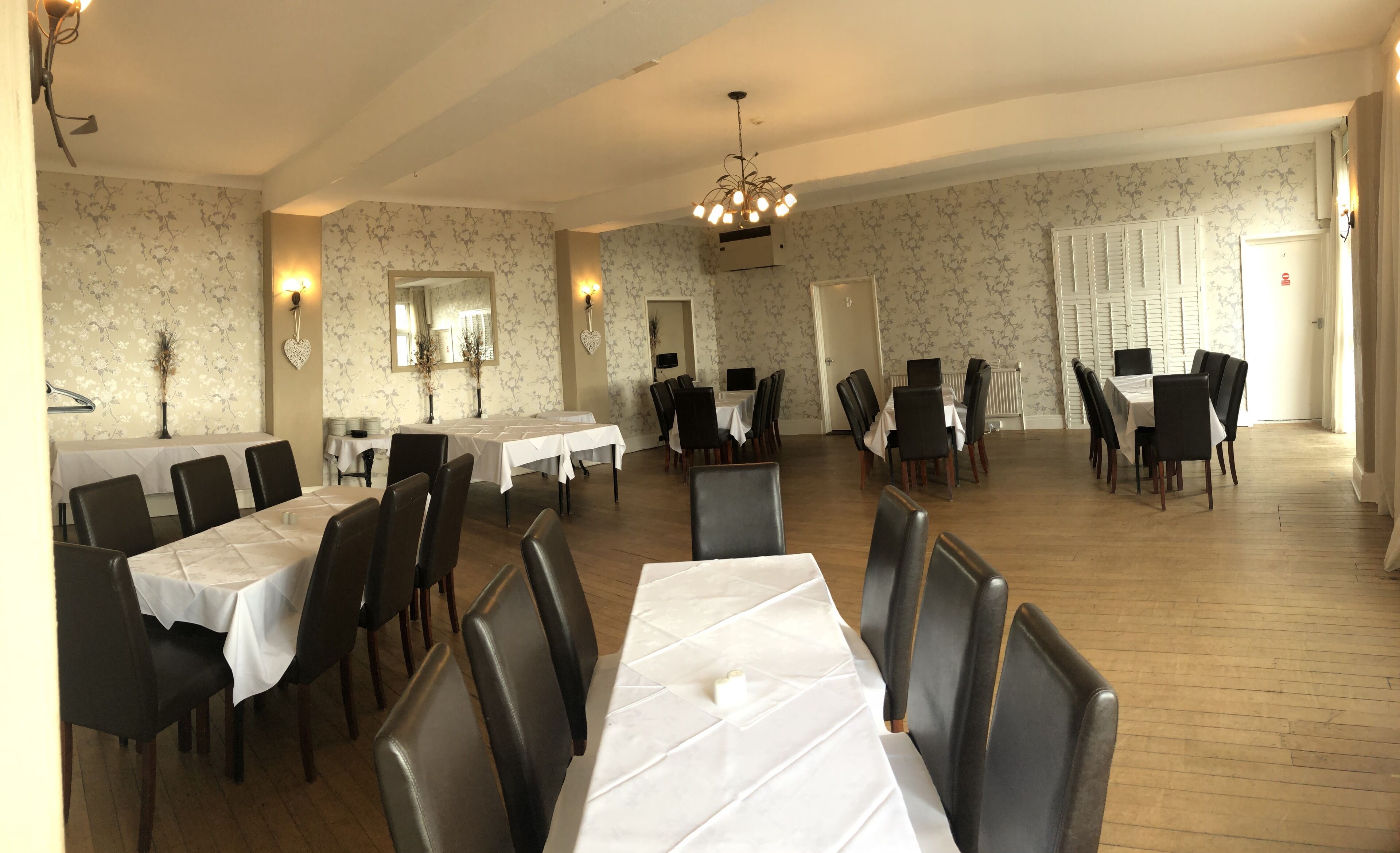 A dining area with multiple tables and chairs, a chandelier, and floral wallpaper.