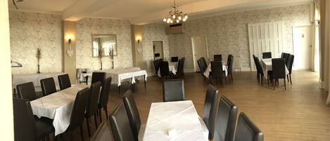 A dining area with multiple tables and chairs, a chandelier, and floral wallpaper.