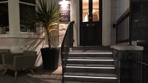 A hotel entrance with a staircase leading to the door, a potted plant, and a wicker chair outside. - Lynton House (Llandudno)