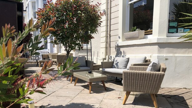An outdoor seating area with wicker furniture, a potted tree, and a building with a window. - Lynton House (Llandudno)