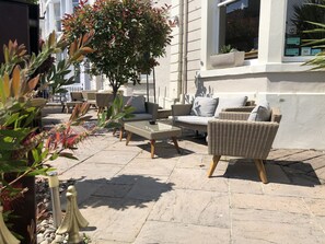 Un espace extérieur aménagé avec des meubles en osier, un arbre en pot et un bâtiment doté d’une fenêtre.