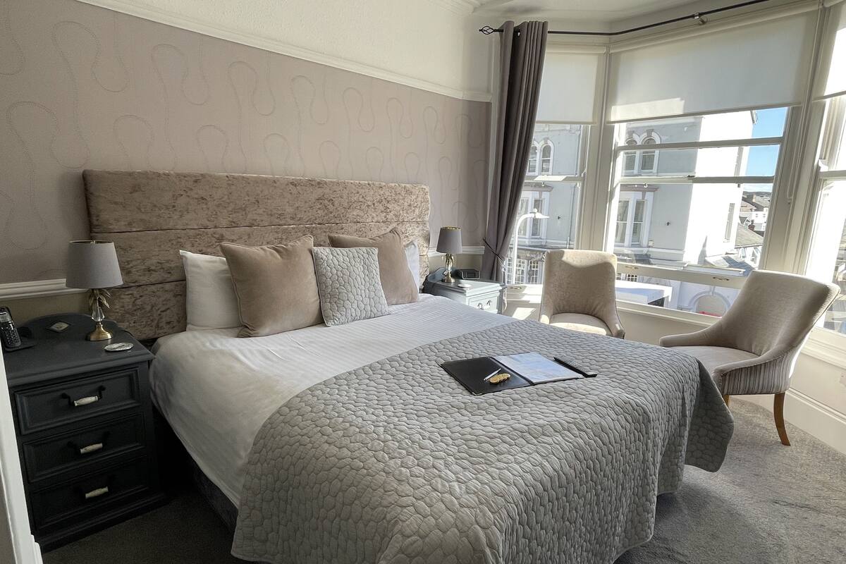 A hotel room with a large bed, a nightstand, a chair, and a view of the city through the window.