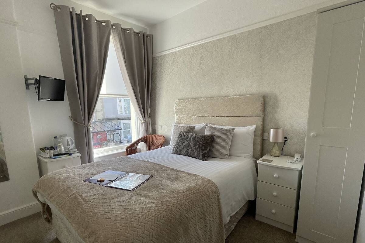 A hotel room with a bed, a chair, a nightstand, a TV, and a wardrobe.