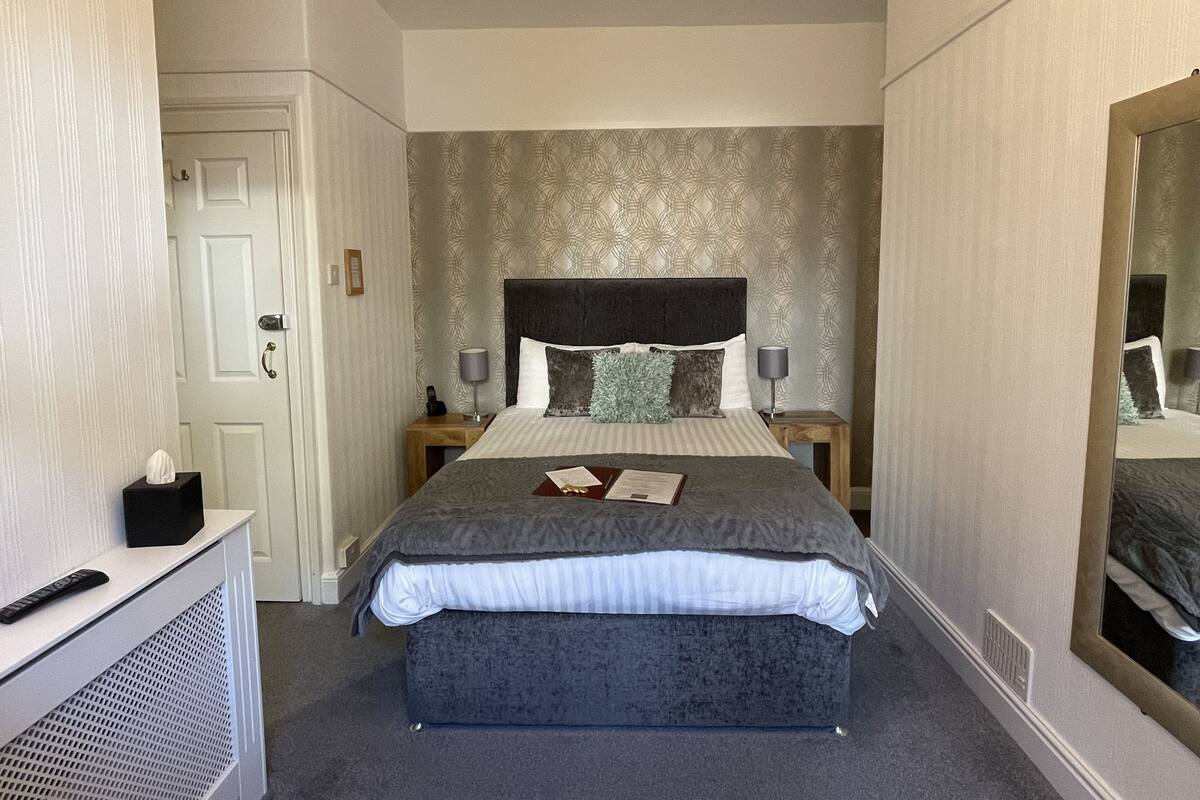 A hotel room with a large bed, two bedside tables with lamps, a bedside telephone, a mirror, and a small bedside table with a tissue box.
