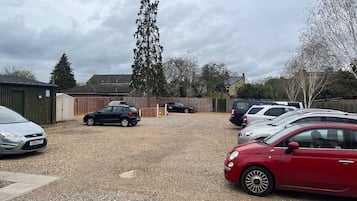 Een parkeerplaats met meerdere auto's, een grindoppervlak en een gebouw op de achtergrond.