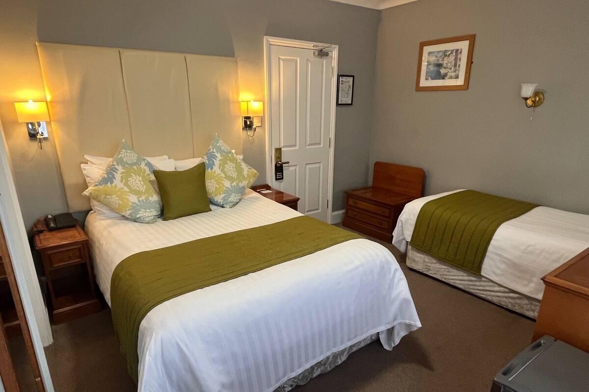 A hotel room with two beds, a nightstand, a dresser, and a door.