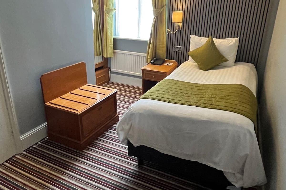 A hotel room with a bed, bedside table, lamp, and a window with curtains.