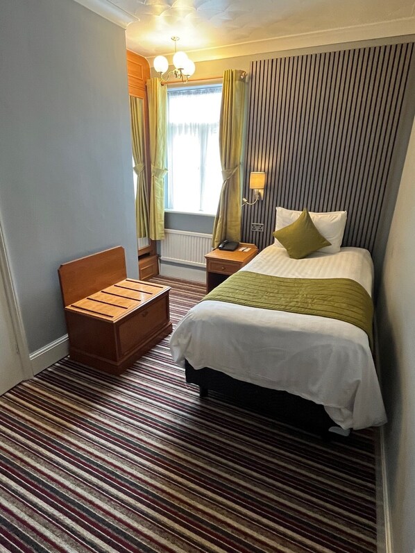 Habitación de hotel con cama, mesita de noche, lámpara y ventana con cortinas.