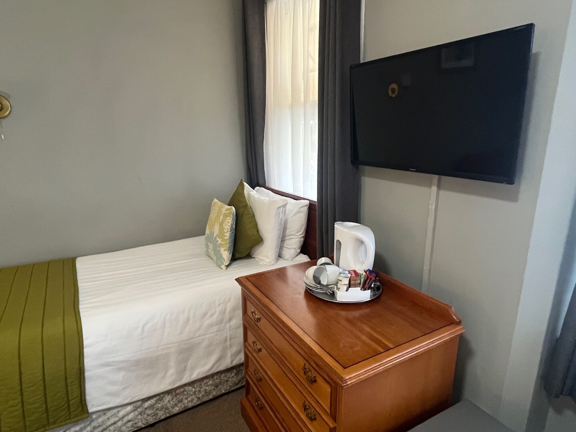 A hotel room with a bed, a wooden nightstand, a coffee maker, and a flat-screen TV.