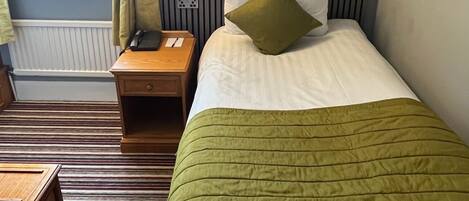 A hotel room with a bed, a nightstand, a lamp, a window with curtains, and a radiator.