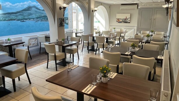 A restaurant with multiple dining tables and chairs, large windows with a view of a mountain and water, and a sign on the wall. - Sorrento Hotel (Cambridge)