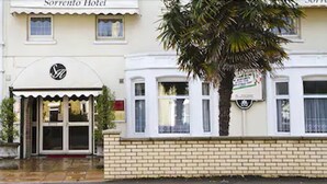 A hotel entrance with a double door, a logo above the door, and a palm tree to the right. - Sorrento Hotel (Cambridge)