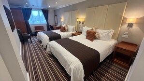 A hotel room with two beds, striped carpet, bedside lamps, and a window with curtains. - Sorrento Hotel (Cambridge)