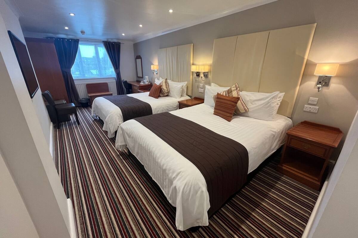 A hotel room with two beds, striped carpet, bedside lamps, and a window with curtains.