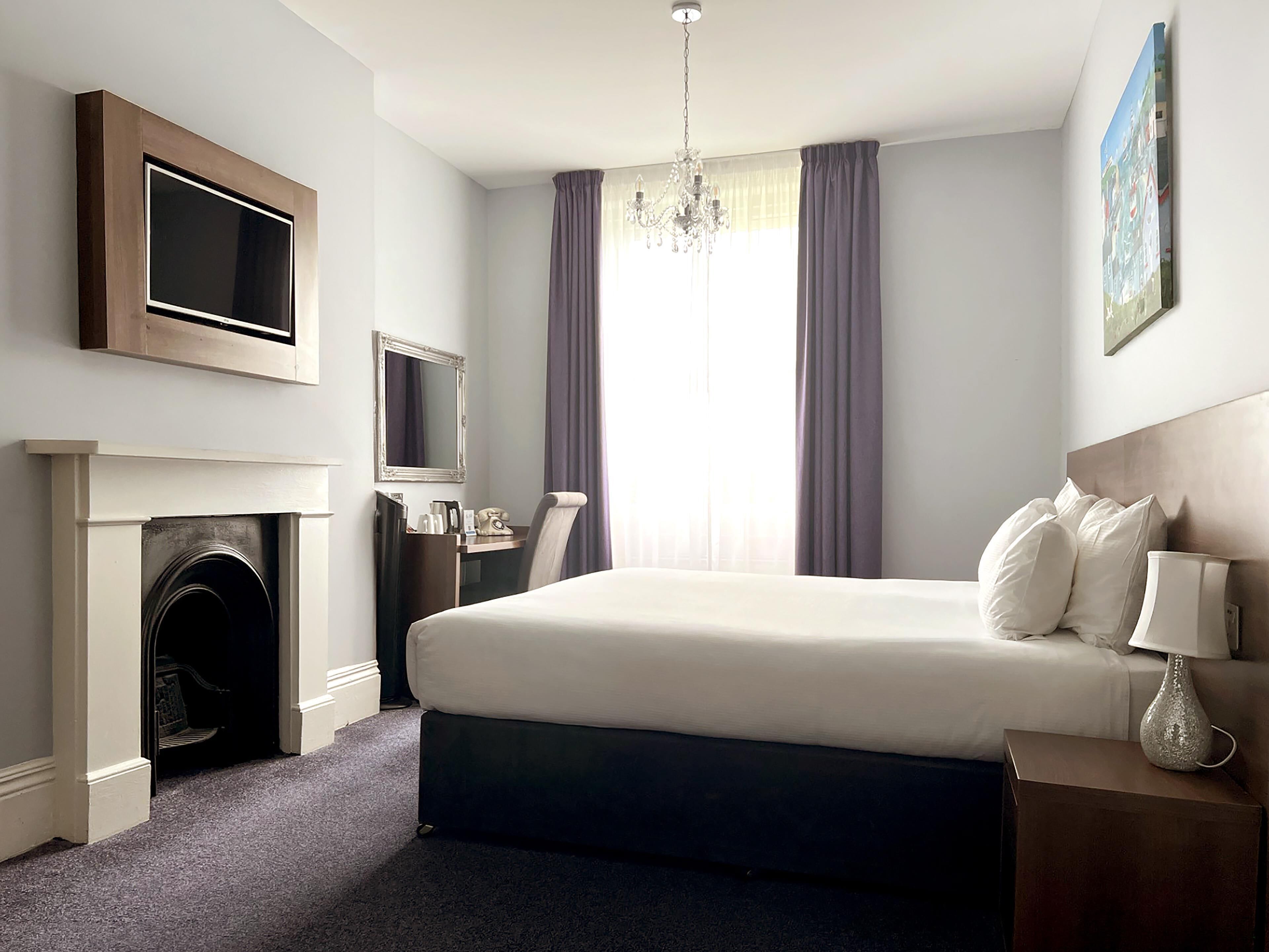 Ein Hotelzimmer mit einem Bett, einem flachbildfernseher darüber, einem Kamin, einem Schreibtisch mit Telefon und einem Nachttisch mit Lampe.