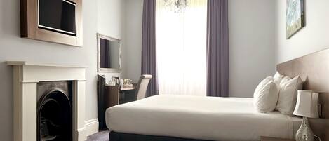 Habitación de hotel con cama, televisor de pantalla plana sobre ella, chimenea, escritorio con teléfono y mesita de noche con lámpara.