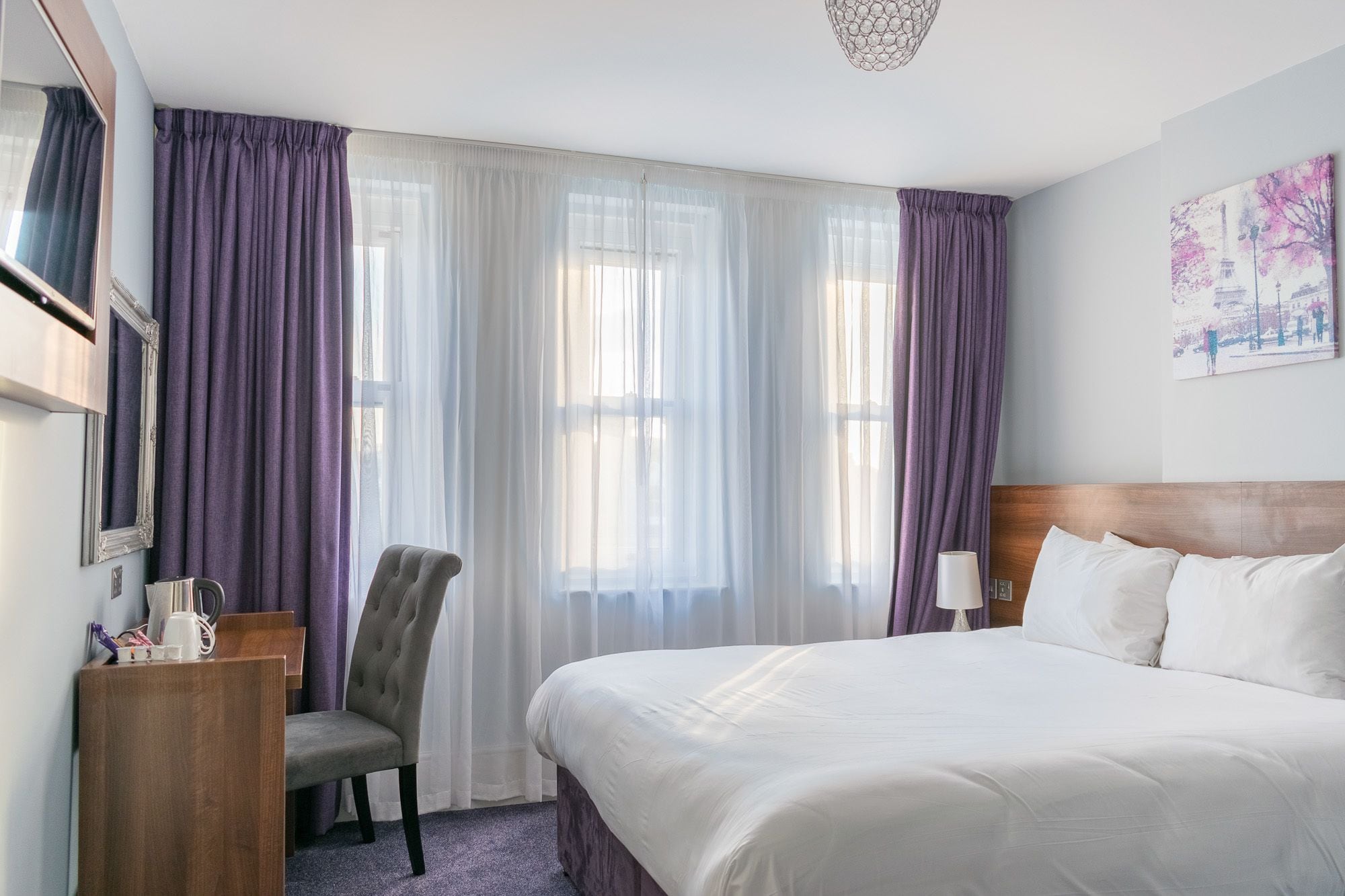 Une chambre d’hôtel avec un grand lit, une chaise, un bureau et une fenêtre avec des rideaux.